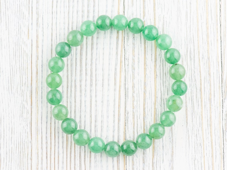 May include: A green gemstone bracelet made of round beads. The bracelet is laid out on a white wooden surface.
