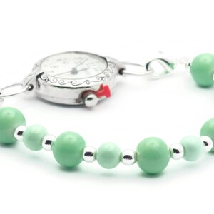 May include: A silver pocket watch with a white face and black hands attached to a bracelet of light green beads.