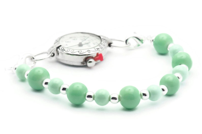 May include: A silver pocket watch with a white face and black hands attached to a bracelet of light green beads.