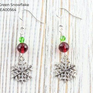 Pode incluir: Brincos de floco de neve prateados com detalhes em vermelho e verde. Cada brinco apresenta um pingente de floco de neve prateado, uma conta vermelha facetada e uma conta verde. O texto "Red & Green Snowflake EA00564" &eacute; vis&iacute;vel.