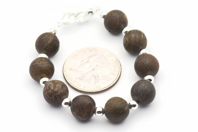 Puede incluir: Un brazalete de cuentas de madera marr&oacute;n con cuentas espaciadoras plateadas. El brazalete es aproximadamente del tama&ntilde;o de una moneda de 25 c&eacute;ntimos.