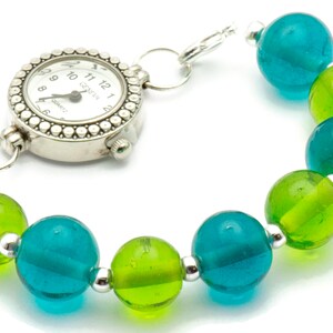 Puede incluir: Un reloj plateado con una esfera blanca y agujas negras unidas a una pulsera hecha de cuentas de vidrio turquesa y verde alternas.
