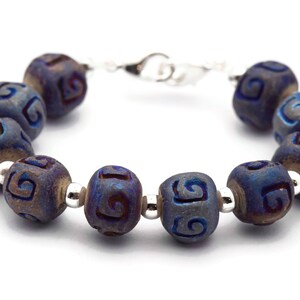 Pu&ograve; includere: Un braccialetto blu e argento con una serie di perline rotonde. Ogni perlina ha un motivo a spirale intagliato.