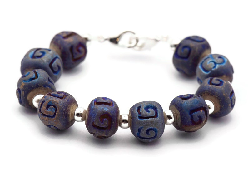 Pu&ograve; includere: Un braccialetto blu e argento con una serie di perline rotonde. Ogni perlina ha un motivo a spirale intagliato.