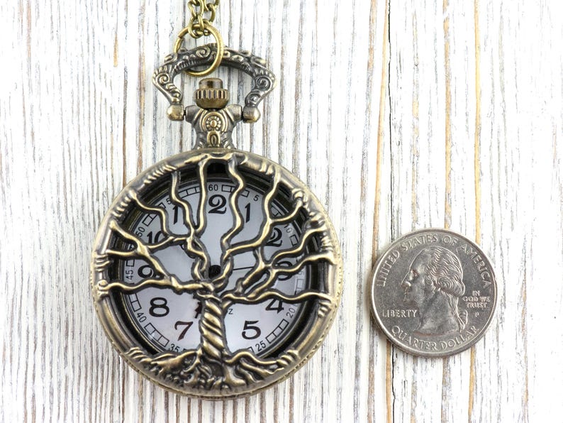 May include: Vintage bronze pocket watch featuring a tree of life motif. The watch face is white with black numerals and hands. A quarter coin is next to the watch for size comparison. The watch's diameter is approximately 4 cm.