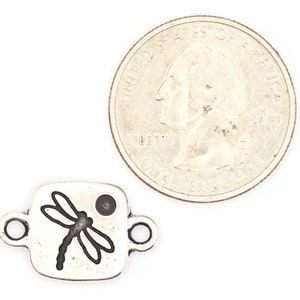 May include: Silver charm with a dragonfly design. The charm is square shaped and has a small hole at the top for attaching to a bracelet or necklace. The charm is about the size of a US quarter.