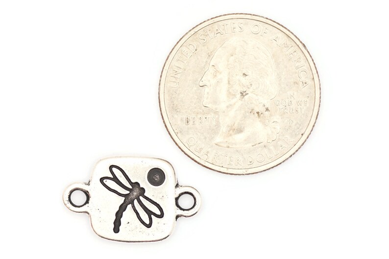 May include: Silver charm with a dragonfly design. The charm is square shaped and has a small hole at the top for attaching to a bracelet or necklace. The charm is about the size of a US quarter.