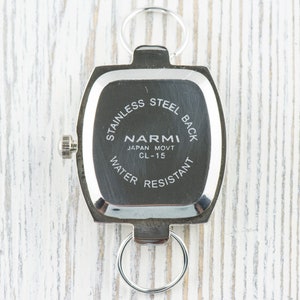 May include: Silver watch back with the text "Stainless Steel Back", "Narmi", "Japan Movt CL-15", and "Water Resistant".
