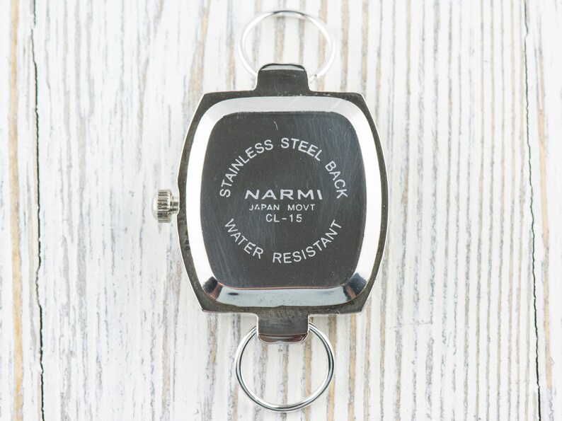 May include: Silver watch back with the text "Stainless Steel Back", "Narmi", "Japan Movt CL-15", and "Water Resistant".