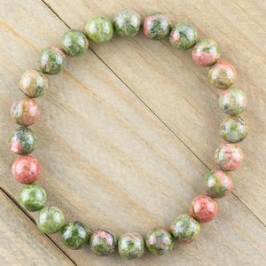 May include: A green, pink, and brown gemstone bracelet with round beads.