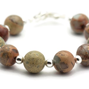 May include: A bracelet made with brown, green, and white patterned beads separated by silver beads.