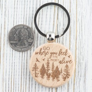 May include: Wooden keychain with a brown background and the text "Go where you feel the most alive" engraved on it. The keychain features a silver key ring and a design of trees.