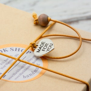 May include: A brown cardboard box with a yellow string tied around it. The string has a silver heart charm with the words "MADE FOR YOU" on it. The box has a round sticker with the text "BLACK BROOK SHOP" and contact information.