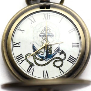 May include: A gold pocket watch with a white face and Roman numeral hour markers. The watch face features a blue anchor with a rope design and a gold compass wheel.