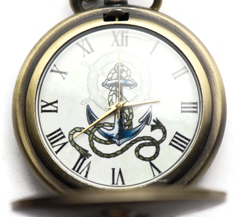 May include: A gold pocket watch with a white face and Roman numeral hour markers. The watch face features a blue anchor with a rope design and a gold compass wheel.