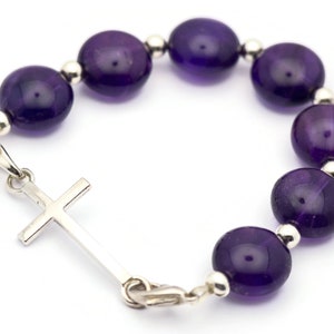May include: A purple amethyst gemstone bracelet with a silver cross charm.