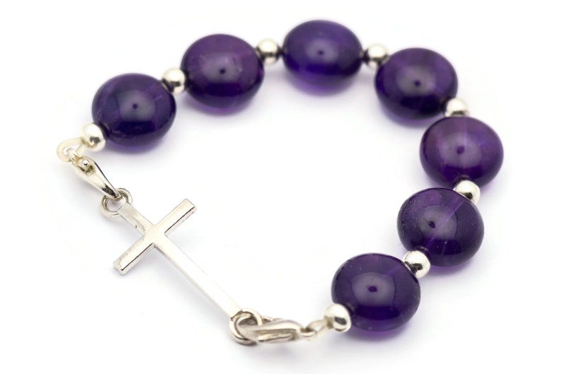 May include: A purple amethyst gemstone bracelet with a silver cross charm.