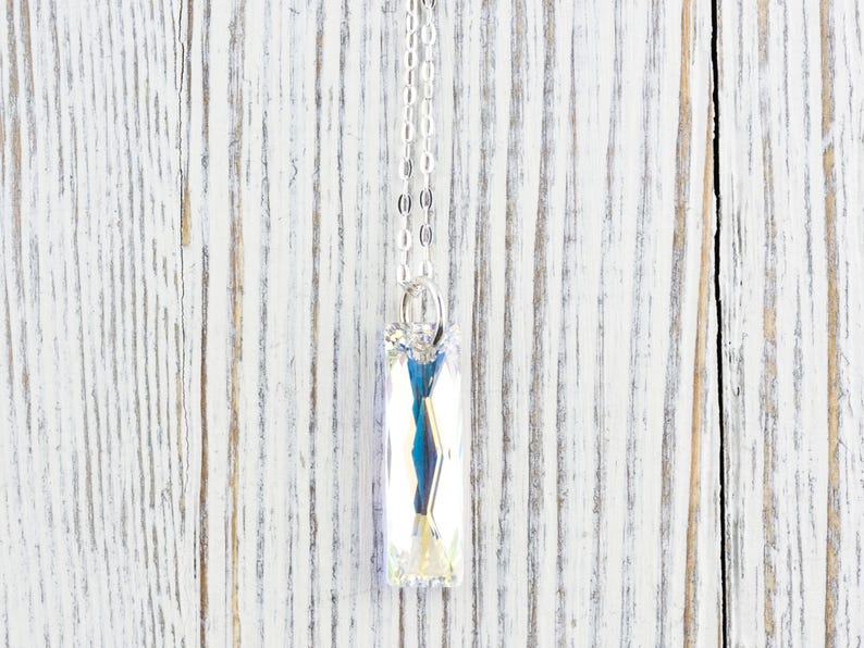 Pu&ograve; includere: Una collana con catena d'argento con un ciondolo di cristallo rettangolare trasparente.