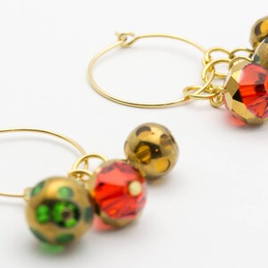 Puede incluir: Aretes de aro de oro con colgantes. Los colgantes son cuentas de vidrio rojo, verde y dorado con un patr&oacute;n moteado.