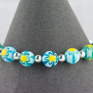 Peut inclure: Un bracelet compos&eacute; de perles de verre bleues et blanches avec des motifs de fleurs jaunes et des perles d'espacement argent&eacute;es.