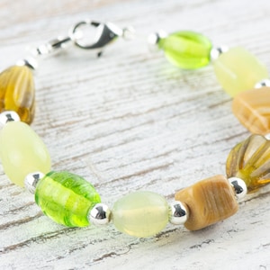May include: A bracelet made with green and brown glass beads and silver spacers. The bracelet has a silver clasp.