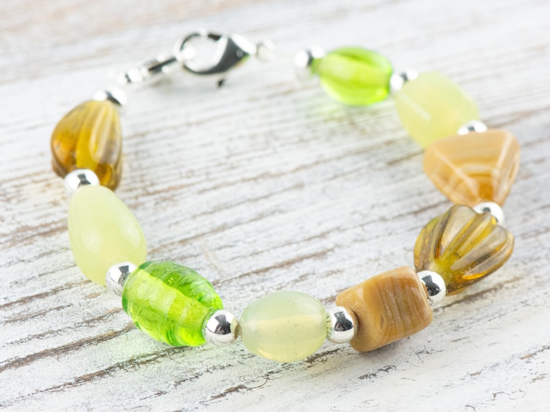May include: A bracelet made with green and brown glass beads and silver spacers. The bracelet has a silver clasp.