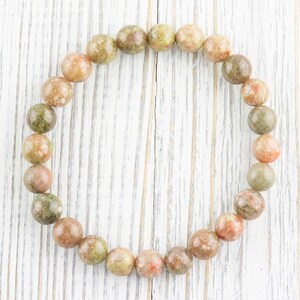 May include: A bracelet made of round, green, pink, and brown speckled stones.