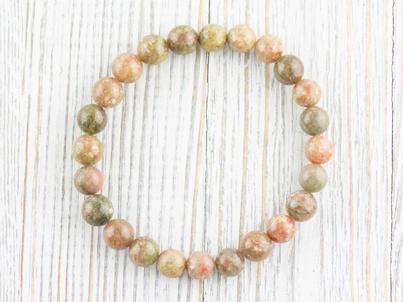May include: A bracelet made of round, green, pink, and brown speckled stones.
