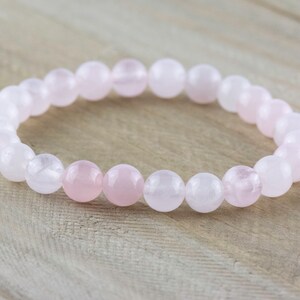 May include: A pink and white gemstone bracelet with round beads. The bracelet is made of rose quartz.