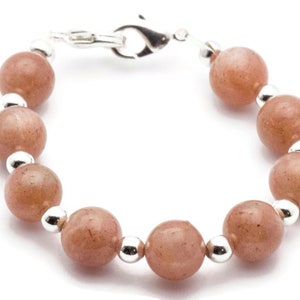 May include: A bracelet made with light brown beads and silver accents. The bracelet has a silver clasp.