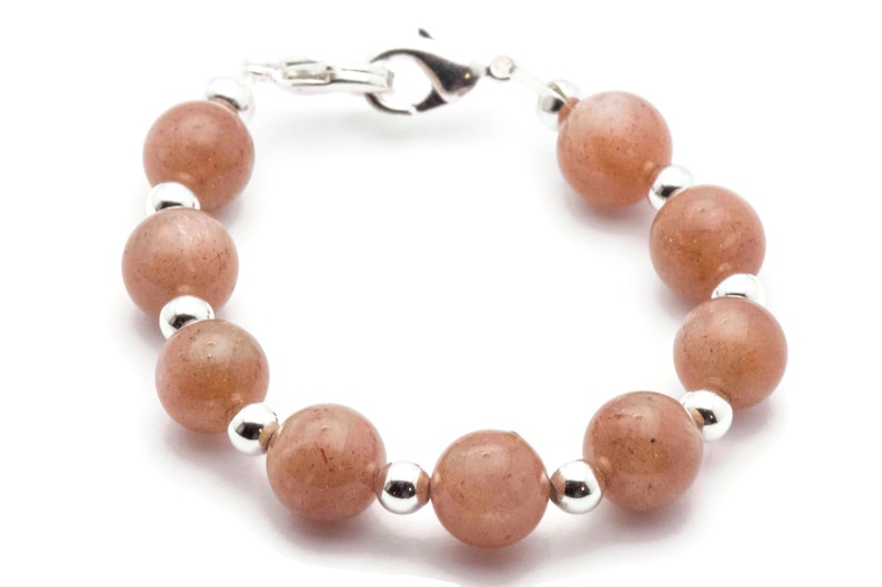 May include: A bracelet made with light brown beads and silver accents. The bracelet has a silver clasp.