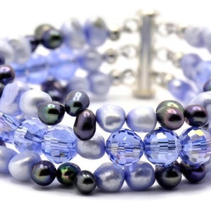 May include: A multi-strand bracelet featuring a mix of blue and black beads. The bracelet is made with glass beads, freshwater pearls, and black pearls.