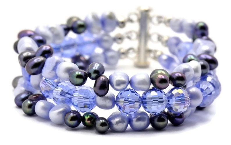 May include: A multi-strand bracelet featuring a mix of blue and black beads. The bracelet is made with glass beads, freshwater pearls, and black pearls.