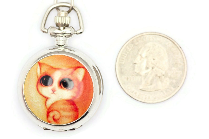 Op de afbeelding: Zilveren zakhorloge met een ketting, met een cartoonkat met oranje en witte vacht en grote ogen. De wijzerplaat van het horloge is oranje en geel.