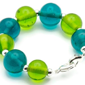 Puede incluir: Un brazalete hecho de cuentas de vidrio verde y azul alternas con un cierre plateado.