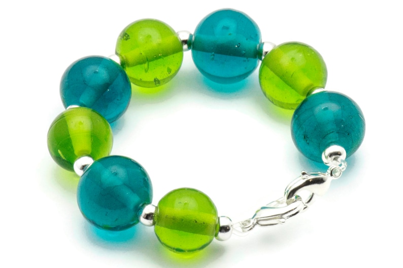 Puede incluir: Un brazalete hecho de cuentas de vidrio verde y azul alternas con un cierre plateado.