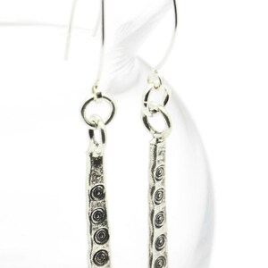 May include: A pair of silver dangle earrings with a textured, hammered design. The earrings feature a series of small, circular patterns along the length of the dangle.