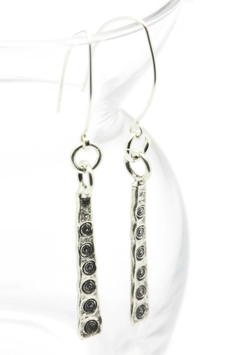 May include: A pair of silver dangle earrings with a textured, hammered design. The earrings feature a series of small, circular patterns along the length of the dangle.