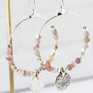 Pu&ograve; includere: Orecchini a cerchio in argento con un ciondolo in argento martellato e perline di agata rosa e grigia.