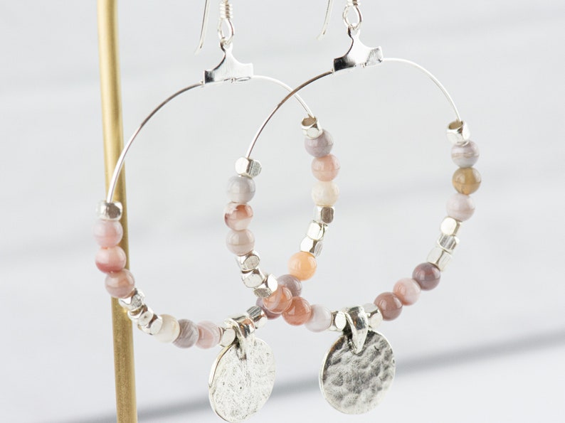 Pu&ograve; includere: Orecchini a cerchio in argento con un ciondolo in argento martellato e perline di agata rosa e grigia.