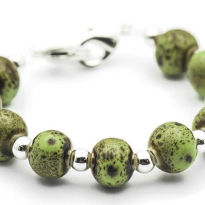 May include: A green and brown speckled bead bracelet with silver accents. The bracelet is made of round beads and has a silver clasp.