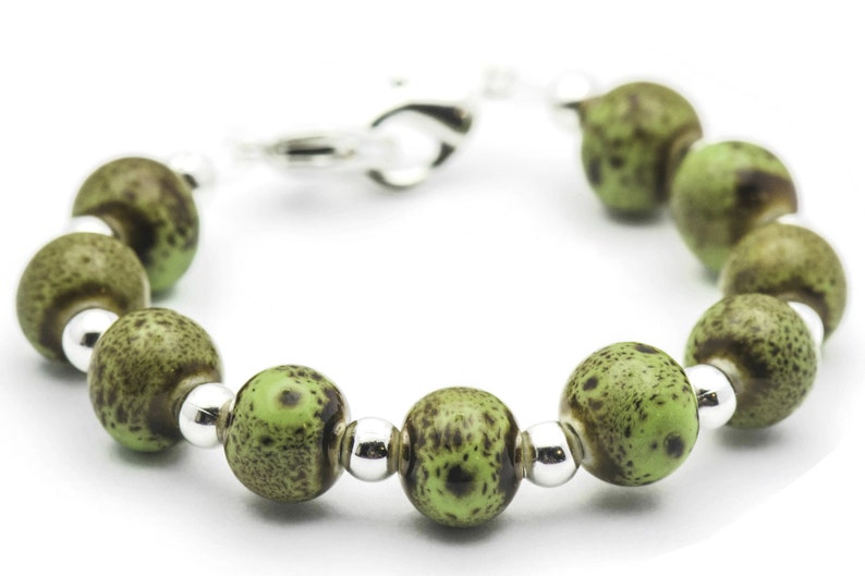 May include: A green and brown speckled bead bracelet with silver accents. The bracelet is made of round beads and has a silver clasp.