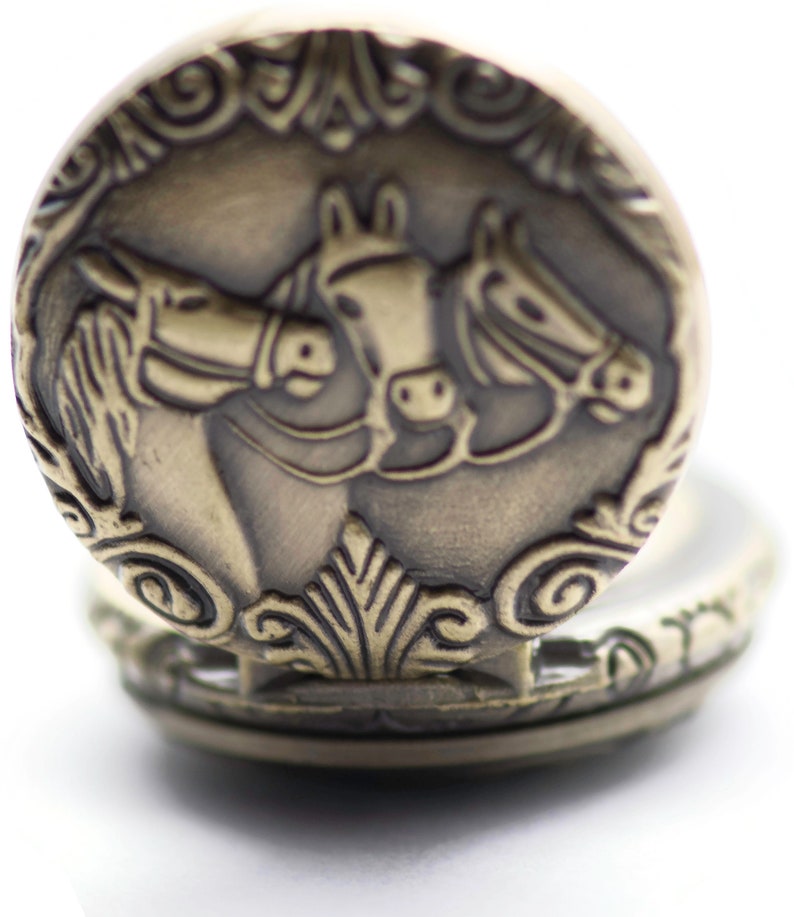 Puede incluir: Un reloj de bolsillo dorado con un dise&ntilde;o ornamentado que presenta dos caballos. La esfera del reloj est&aacute; oculta detr&aacute;s de la tapa.