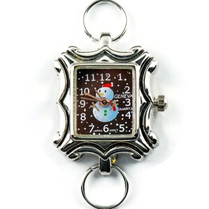 May include: A silver pocket watch with a brown face and a snowman design. The watch face reads "GENEVA QUARTZ" and "JAPAN MVT".
