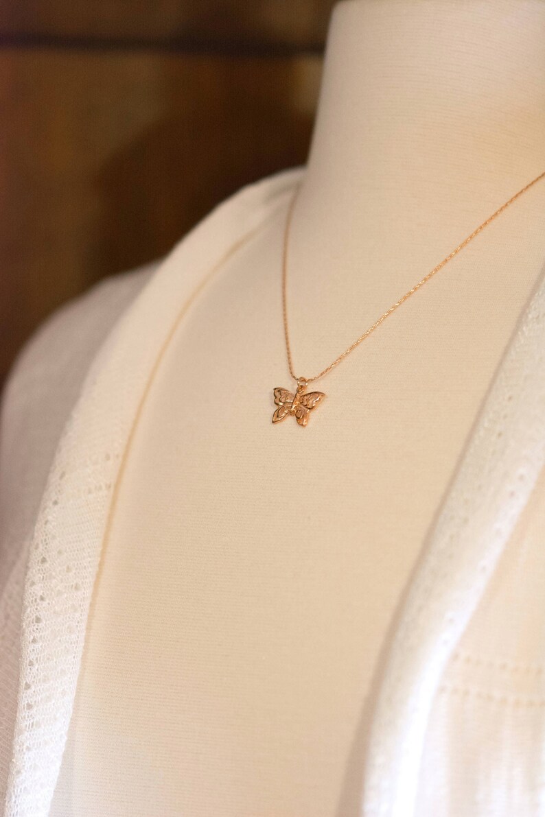 Peut inclure: Un collier avec un pendentif en forme de papillon dor&eacute; sur un mannequin blanc.