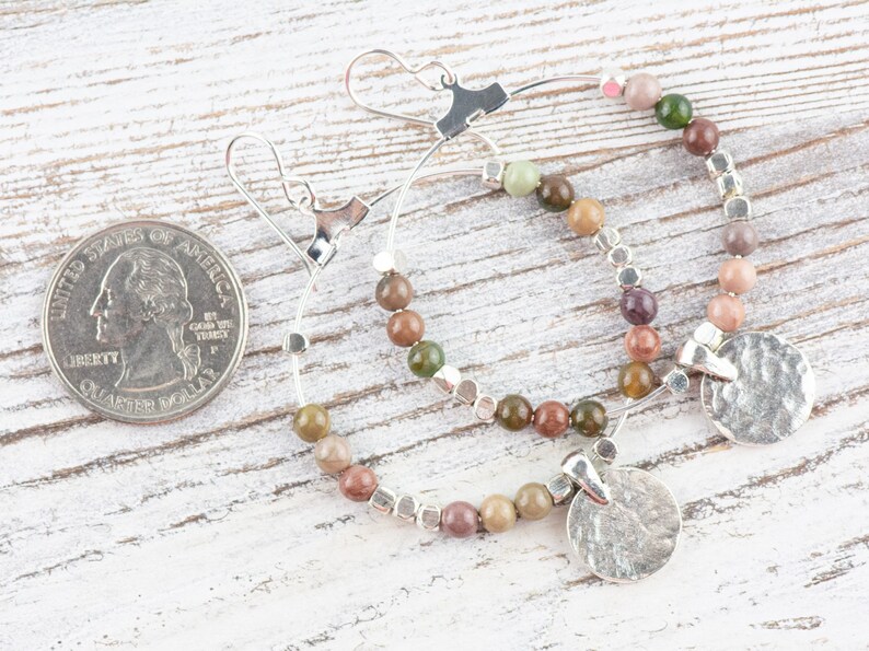 May include: A pair of silver hoop earrings with a hammered silver disc charm. The hoops are adorned with multi-colored gemstone beads.