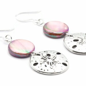 Puede incluir: Un par de pendientes de plata con una concha rosa iridiscente y un dije de d&oacute;lar de arena plateado.
