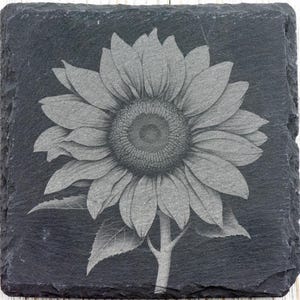 K&ouml;nnte beinhalten: Ein schwarzes und wei&szlig;es, graviertes Bild einer Sonnenblume auf einem schwarzen Schieferuntersetzer.