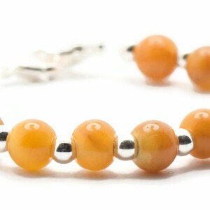 May include: A bracelet made of orange gemstone beads and silver spacers. The bracelet has a clasp closure.