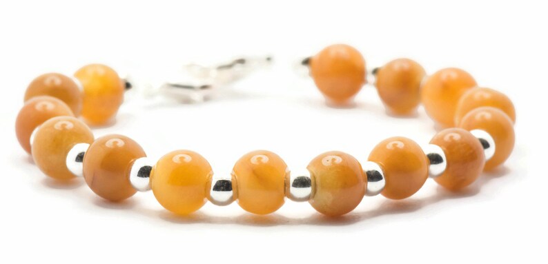 May include: A bracelet made of orange gemstone beads and silver spacers. The bracelet has a clasp closure.